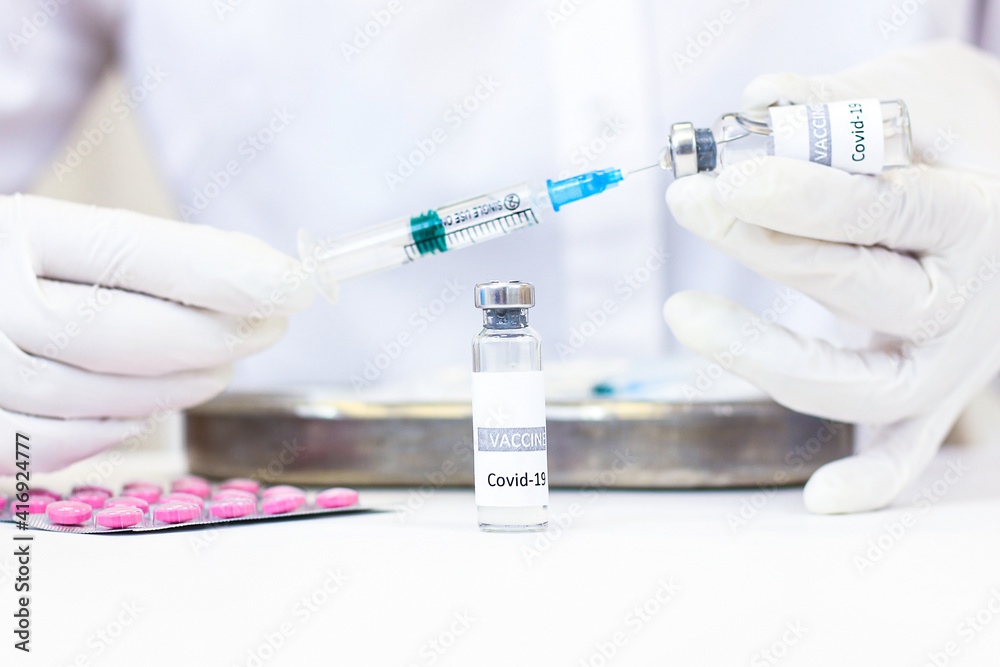 A syringe with a vaccine is held in hands. A vial with a vaccine is on the table A syringe with a vaccine is held in hands. A vial with a vaccine is on the table