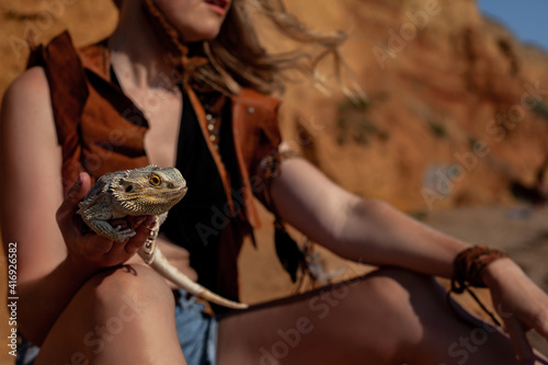 Beautiful woman dressed cowboy style clothes posing with lizard against the camel background. Bearded agam the home pet of girl walking in the nature with owner photo