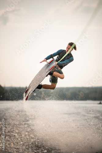 handsome man jumps spectacularly on wakeboard above the water with splashes