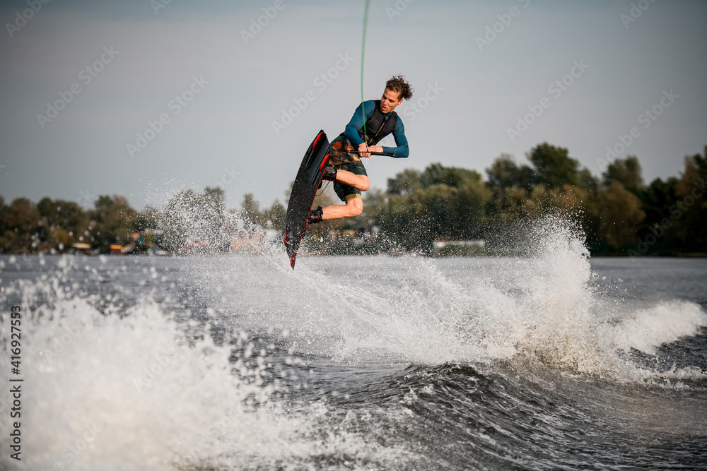 Naklejka premium young adult guy skillfully jumps on wakeboard above the splashing river wave