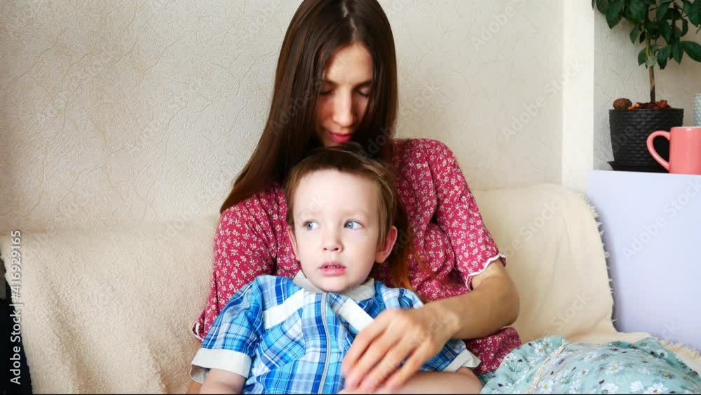 A beautiful woman caresses her lovely little son and kisses him sitting on the soft sofa close-up A beautiful woman caresses her lovely little son and kisses him sitting on the soft sofa close-up