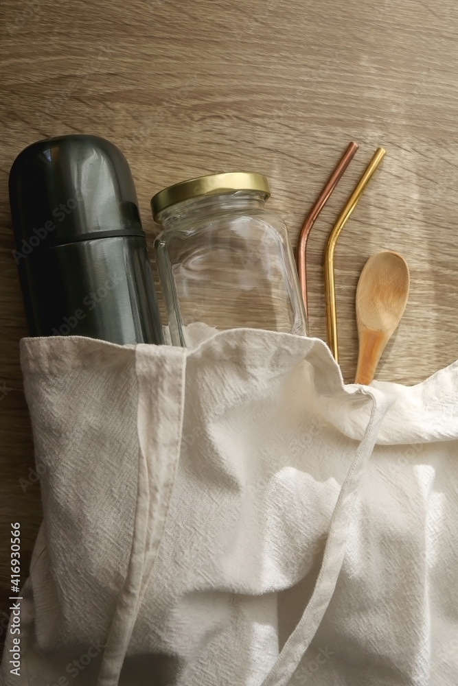 Sustainable kitchen in linen tote bag: thermos bottle, mason jar, wooden spoon and metal straws. Top view. Sustainable kitchen in linen tote bag: thermos bottle, mason jar, wooden spoon and metal straws. Top view.