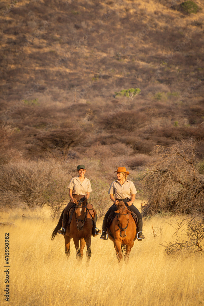 Two women ride through grassland near hill Two women ride through grassland near hill