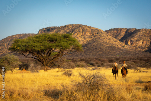 Two women ride through savannah near hills