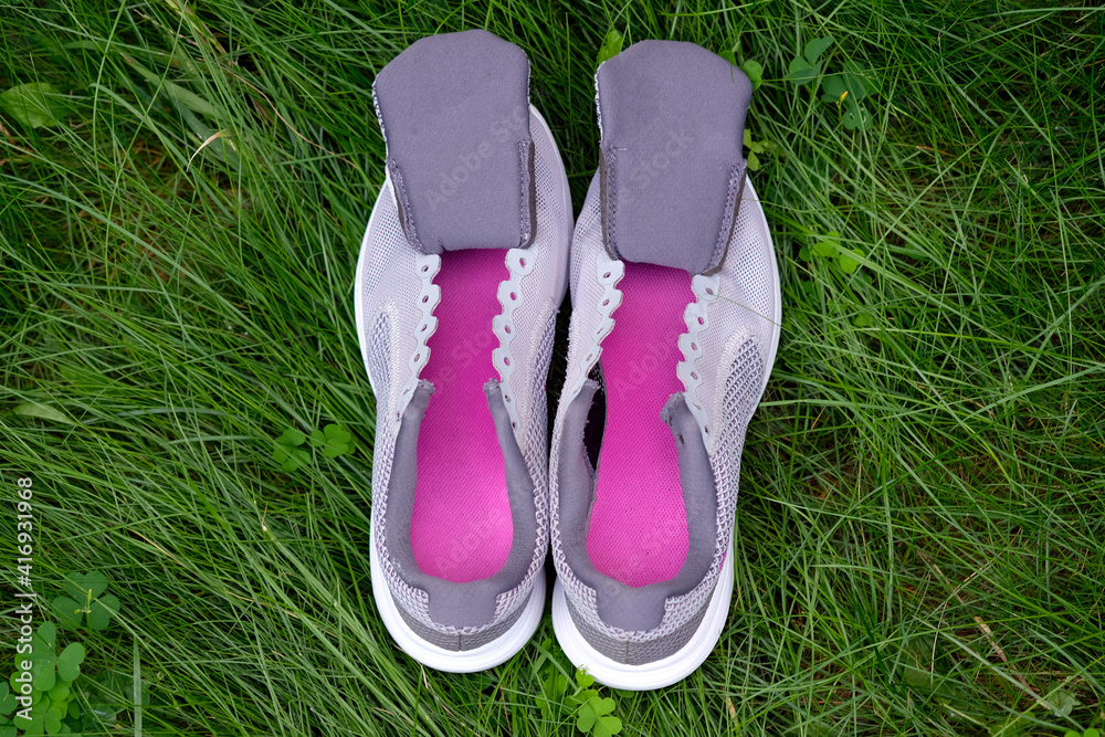 Gray sneakers with tongues top view. Women's sneakers without laces with crimson insoles on a background of green grass. Washing your sneakers after running.