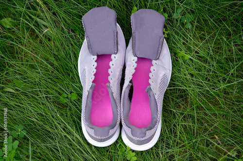 Gray sneakers with tongues top view. Women's sneakers without laces with crimson insoles on a background of green grass. Washing your sneakers after running.