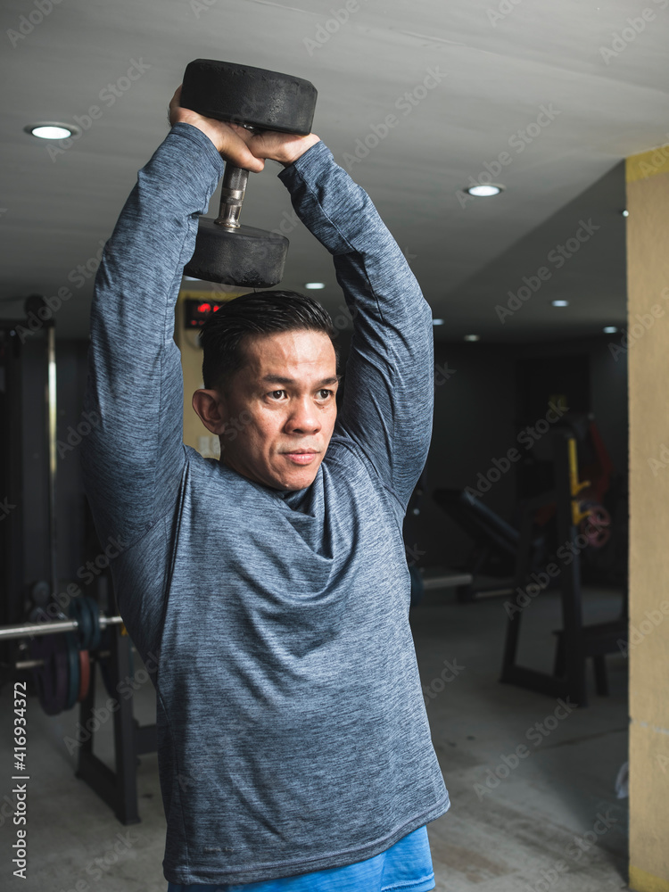 A fit athletic asian guy in a sweatshirt does standing overhead