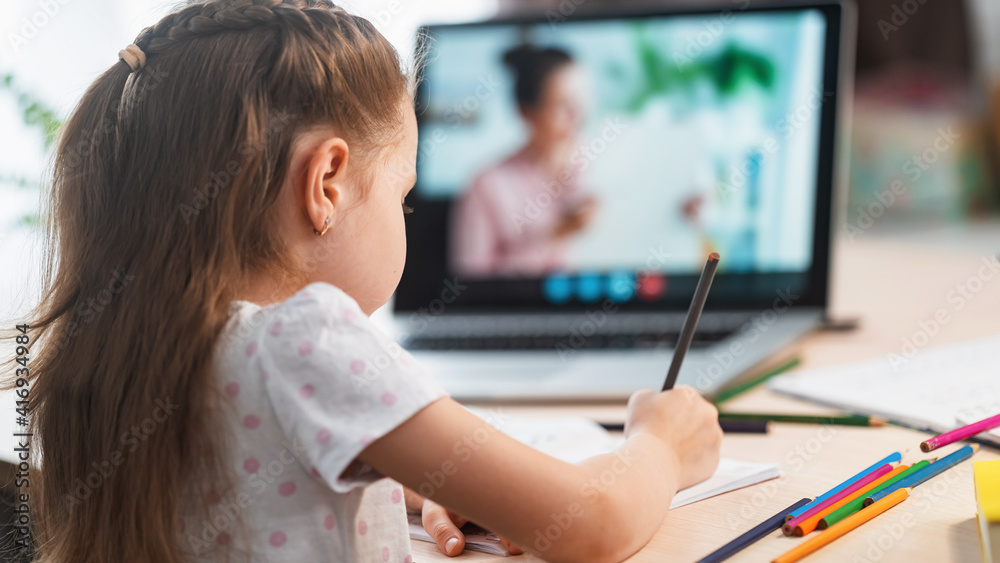 little girl, a preschooler, uses a laptop to study at home. the child smiles happily and receives knowledge remotely. digital concept of e-learning. Distance e-learning. View from over the shoulder little girl, a preschooler, uses a laptop to study at home. the child smiles happily and receives knowledge remotely. digital concept of e-learning. Distance e-learning. View from over the shoulder