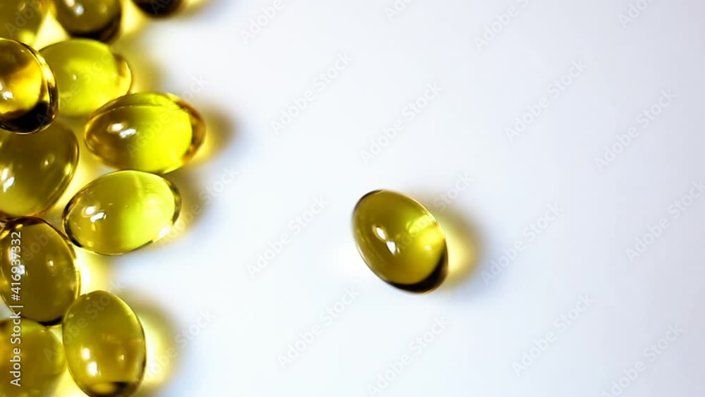 a small oval transparent yellow capsule rotates on a white background. Real-time, close-up medical supplies.