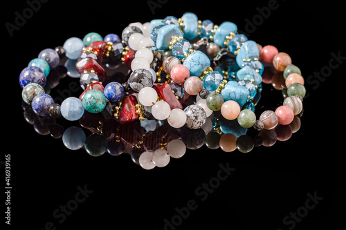 Close-up view to handmade beads and gems bracelet on black. Blue, red and pink stone.  © Alexey Alikeev