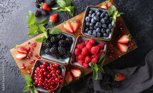 Fresh berries. Red currants, blackberries, blueberries and raspberries in bowls on a large wooden board with mint leaves, strawberries and pomegranate seeds. Background image, top view, horizontal