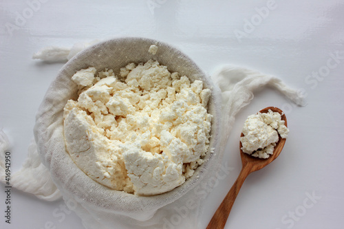 Close-up of freshly made white soft cottage cheese in bowl on white table background. Homemade ricotta in cheesecloth. Top view
