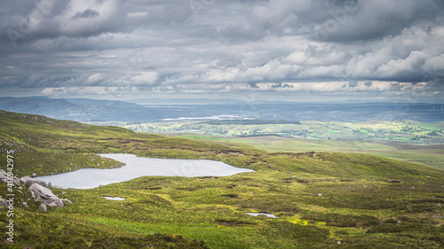 Green fields or rolling hills with small lake at footstep of Cuilcagh Mountain, dramatick stormy sky in background, Northern Ireland photo