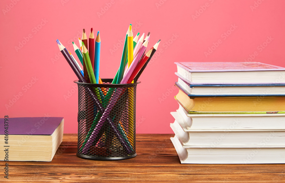Fototapeta premium A stack of books, colored pencils on a pink background.