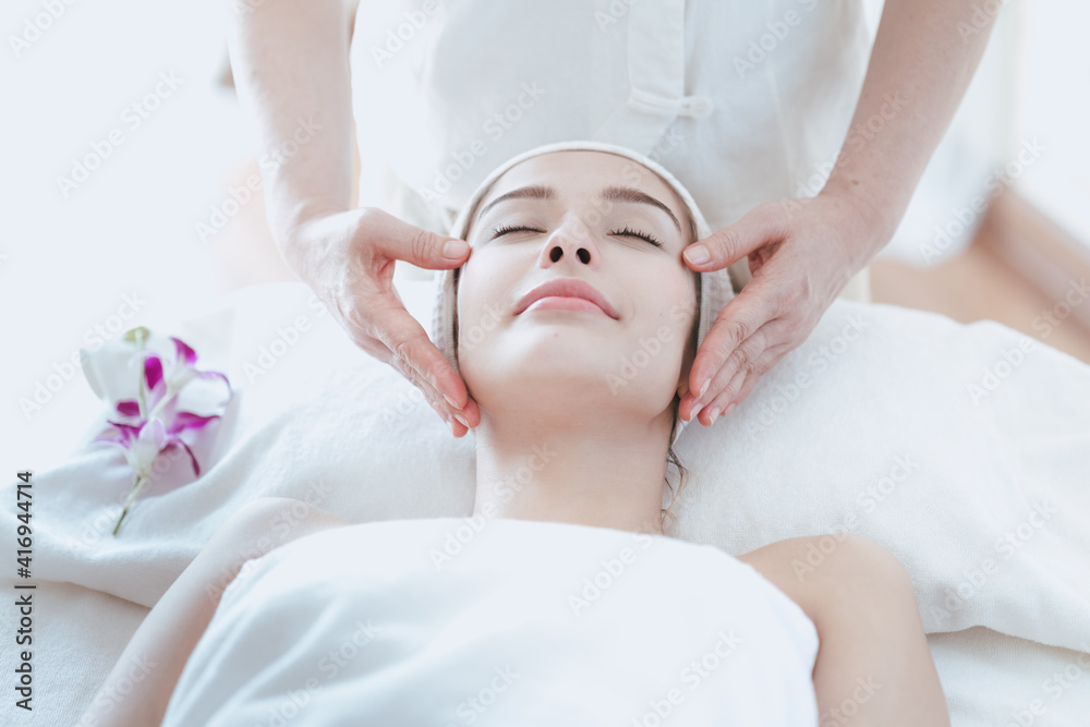 Female massage therapist giving a massage at a spa. Young woman receiving head and facial massage in spa salon.