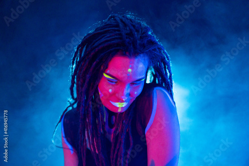 Cocky Girl with Dreadlocks in Ultraviolet neon light with Foggy Background. Bodyart