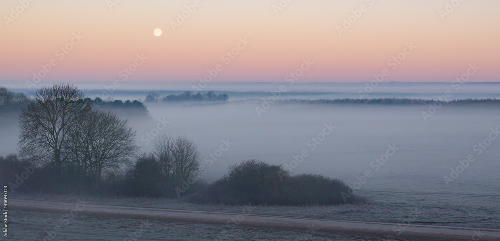 an early morning mist filled valley with the snow moon low in the sunrise sky an early morning mist filled valley with the snow moon low in the sunrise sky