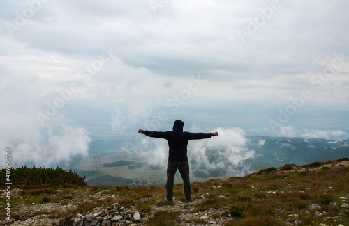 The hiker standing with raised hands on a top of mountain and enjoying the view of cloudy valley. Back view. Outdoor activity  lifestyle concept