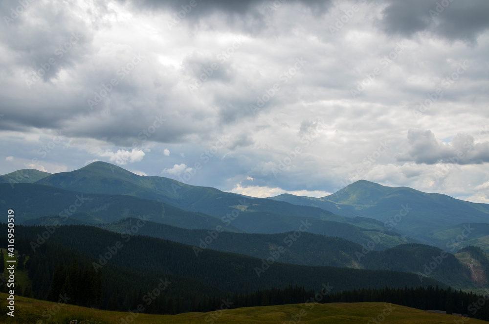 Panorama view of peaks ridge, mountains covered with green forest under cloudy sky. Carpathians, Ukraine Panorama view of peaks ridge, mountains covered with green forest under cloudy sky. Carpathians, Ukraine