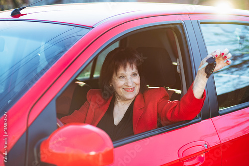 An elderly woman was presented with a red car. Grandma holds keys and smiles