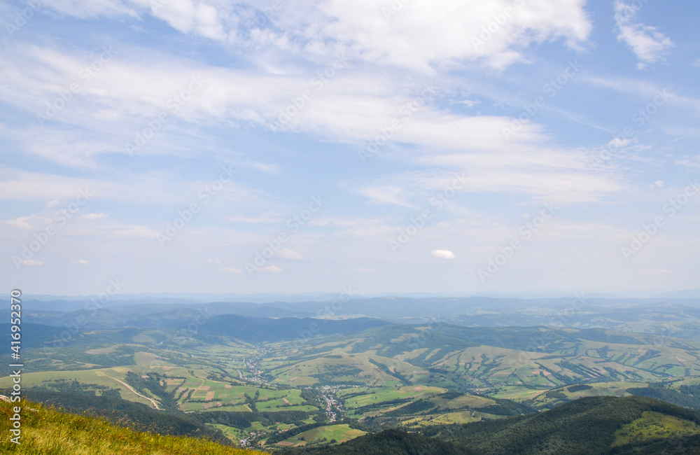 Summer landscape from the height to green forest and picturesque village in the valley against the blue sky. Carpathian Mountains, Ukraine