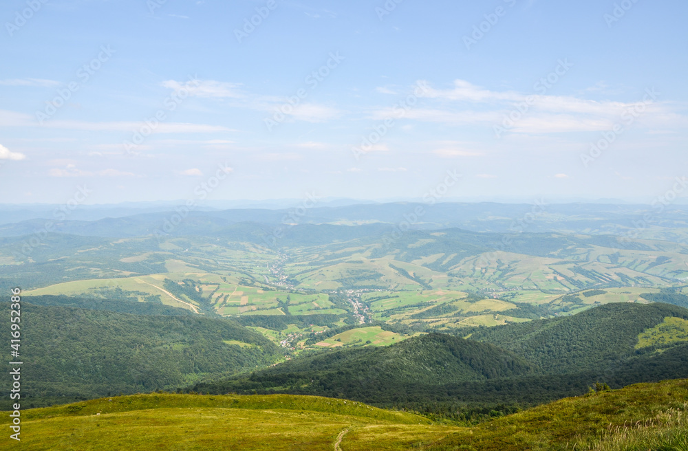 Summer landscape from the height to green forest and picturesque village in the valley against the blue sky. Carpathian Mountains, Ukraine