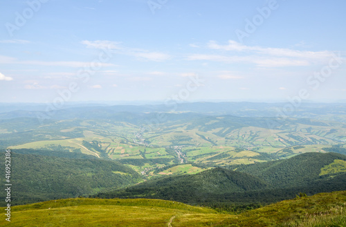 Summer landscape from the height to green forest and picturesque village in the valley against the blue sky. Carpathian Mountains, Ukraine
