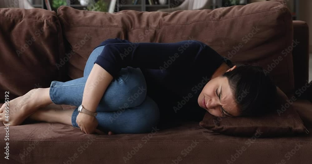 Depressed young indian ethnicity woman lying on sofa in living room, feeling stressed after divorce or relations breakup, unhealthy mixed race lady suffering from abdominal or stomach ache indoors. Depressed young indian ethnicity woman lying on sofa in living room, feeling stressed after divorce or relations breakup, unhealthy mixed race lady suffering from abdominal or stomach ache indoors.