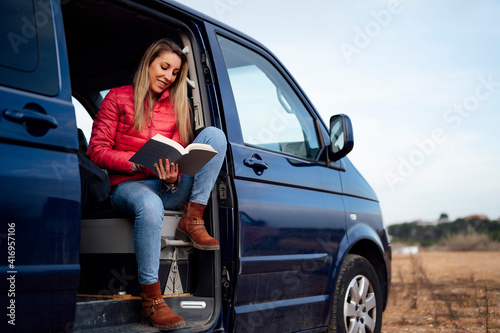 Happy woman reading book on door of camper van