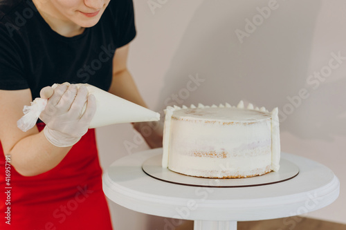 Chef or baker decorating cake with white whipped cream.