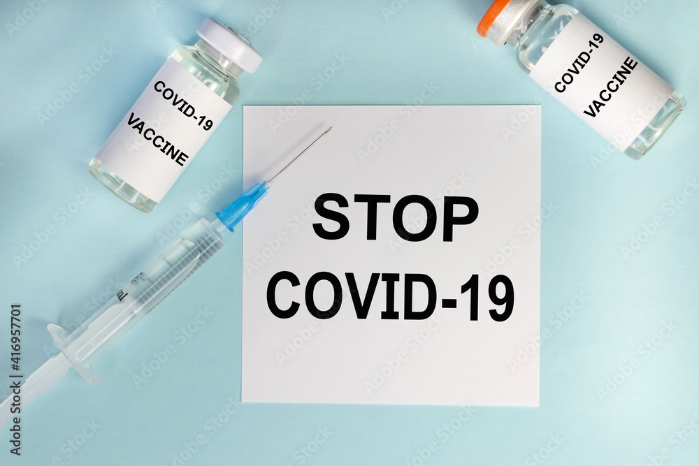 Obraz premium On a blue background among the ampoules and a syringe there is a white sheet on which the inscription stop covid-19. Medical concept. Vaccination of the population