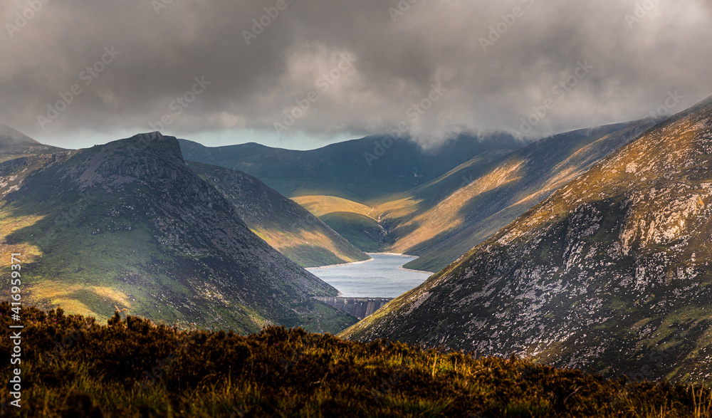 Ben Crom reservoir in The Silent Valley with sun patches lighting up the flanking mountains as low cloud starts to roll in. Mountains of Mourne, County Down, Northern Ireland