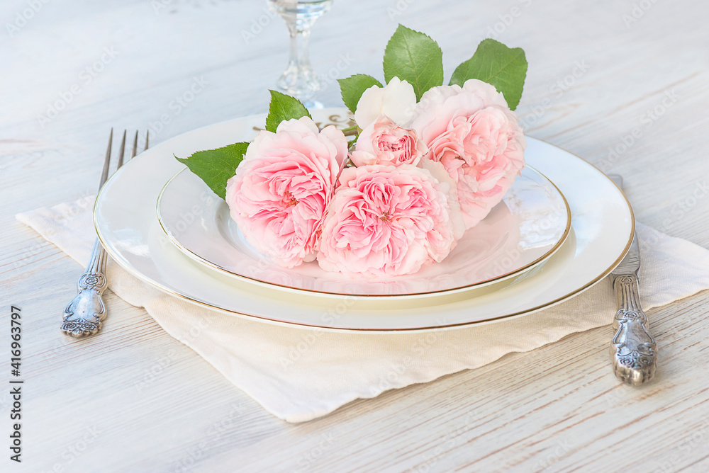 Beautiful place setting with bouquet of pink roses on white plates and vintage fork, knife and wineglass. Close up