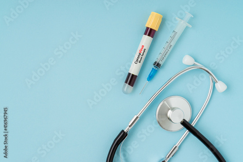 Syringe, stethoscope and blood sample vacuum tube on blue background. Corona virus concept with a copy space.