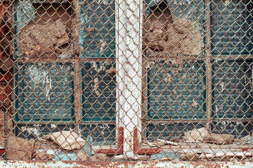 Old broken window with a rusty metal grate. An old broken window behind an iron mesh