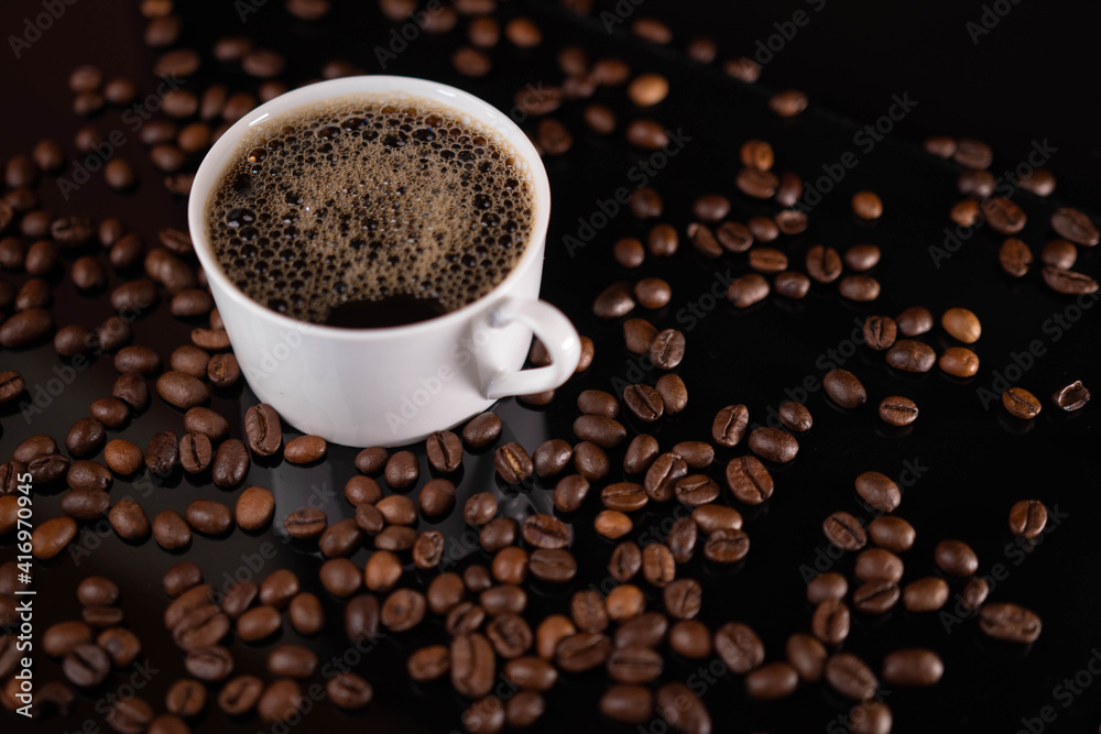 Roasted coffee beans and white mug on black background Roasted coffee beans and white mug on black background