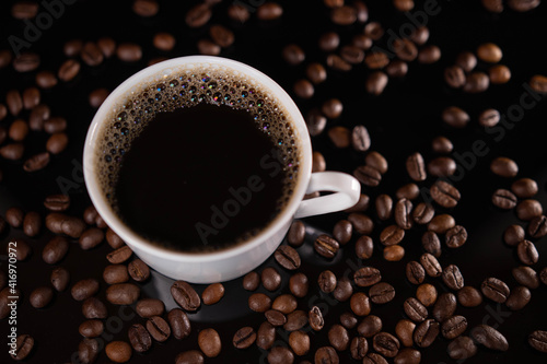 Roasted coffee beans and white mug on black background