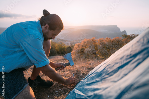 Young male tourist puts a tent in the mountains.