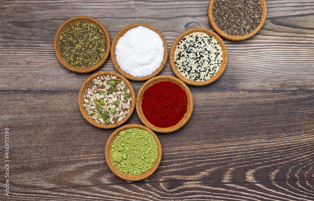 Set of spices, herb and different healthy seeds in wood bowls on brown wood backdrop. Non-symmetric flat lay of brights colors.