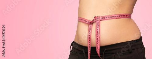 Overweight woman with tape measure around waist. Woman measuring her waistline fat tummy