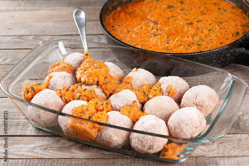 Frozen raw meatballs from beef and pork with carrots and rice in sauce on a woden table photo