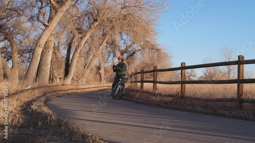 senior male is biking on Poudre River Trail in northern Colorado, fall or winter scenery, stopping for water drinking photo