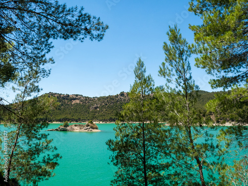Small island in the middle of El Chorro lake in Malaga, close to Alora. Turquoise water and pine trees