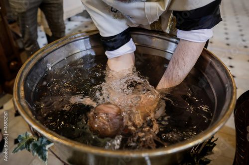 Billede på lærred Details with a baby sunk in the baptismal font by an Orthodox priest during the baptism ceremony