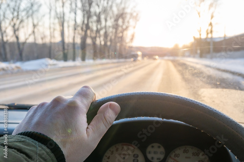 the driver's hand on the steering wheel of a car that is driving on a slippery winter road and the rays of the morning sun make it difficult to see the path, blind the eyes