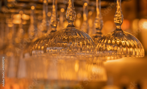 Hanging crystal wine glasses at a bar with golden lights and soft background photo