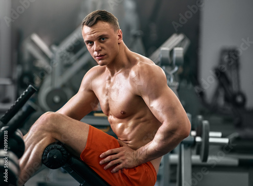 Portrait of young handsome smiling muscular athlete resting in gym