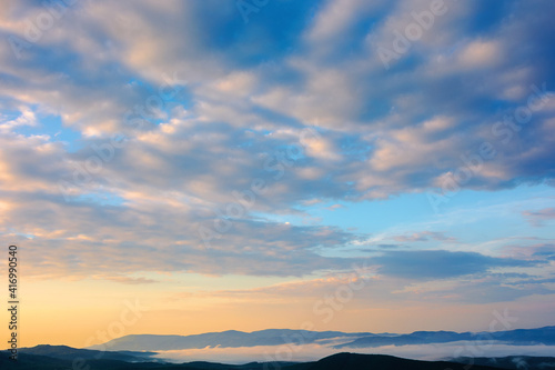cloudscape in summer at sunrise. clouds on the blue sky in yellow and pink morning light. idyllic weather condition, picturesque scenery above the mountain ridge © Pellinni