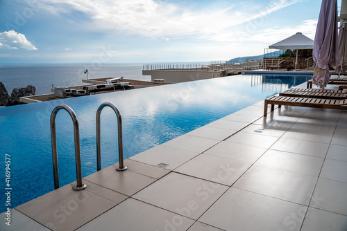 Luxury infinity pool and wooden deck chairs at the resort with beautiful sea views. The concept of recreation, tourism. © svetograph