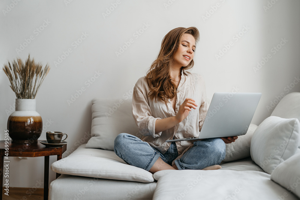 Happy smiling woman sitting on couch and using laptop at living room at home, watching funny video, learning language, video calling, mother working online Happy smiling woman sitting on couch and using laptop at living room at home, watching funny video, learning language, video calling, mother working online